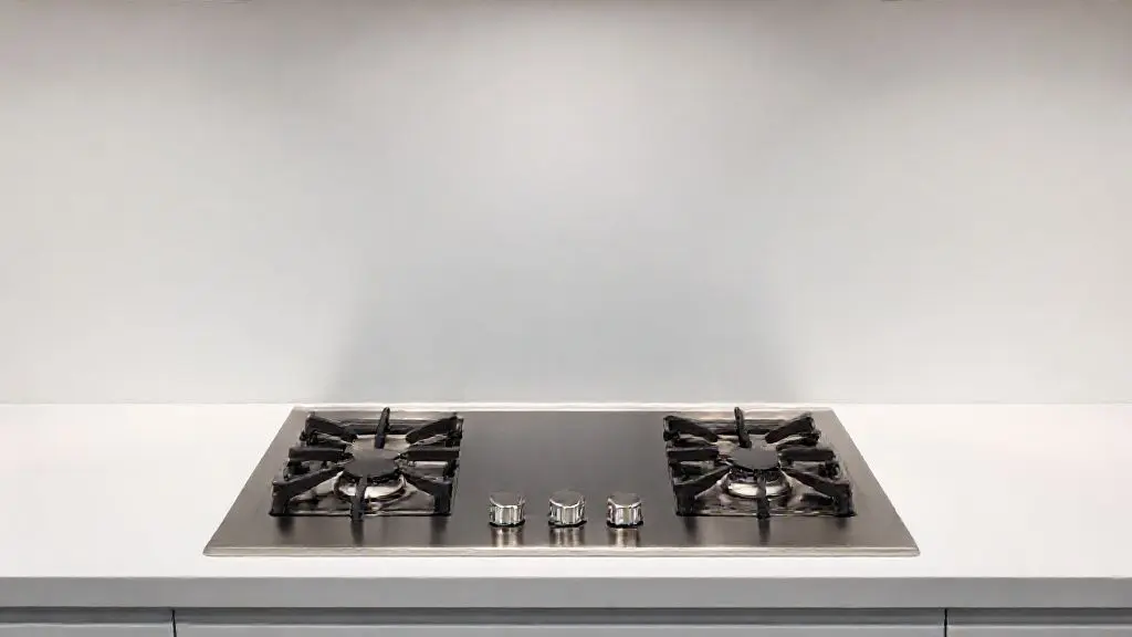 Fogão de embutir moderno em aço inoxidável com queimadores e mesa de vidro preta, integrado a uma bancada de cozinha de design minimalista.